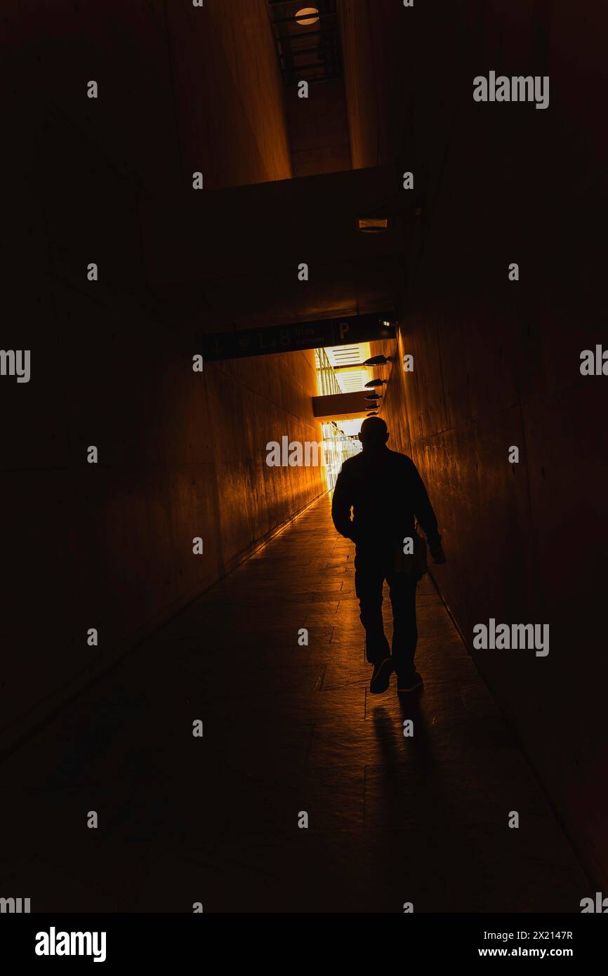 Un uomo cammina lungo un corridoio buio con una luce che gli splende di fronte. Il corridoio e' vuoto e l'uomo e' l'unica persona sulla scena. La scena è inquietante Foto Stock