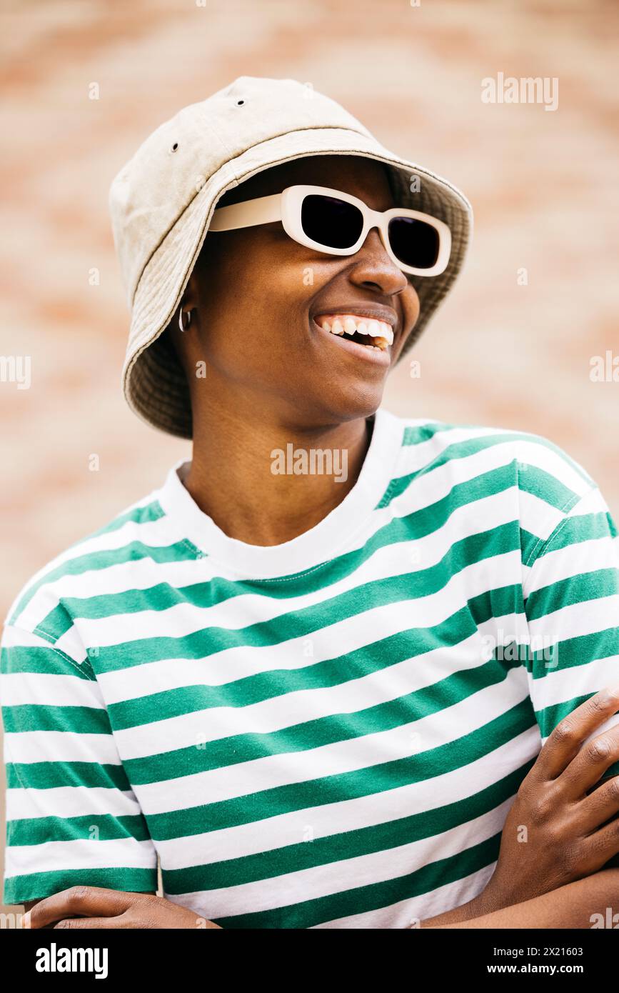 Ritratto all'aperto di una giovane donna allegra che indossa occhiali da sole e un cappello. Giovane donna sorridente allegramente in un ambiente all'aperto. Foto Stock