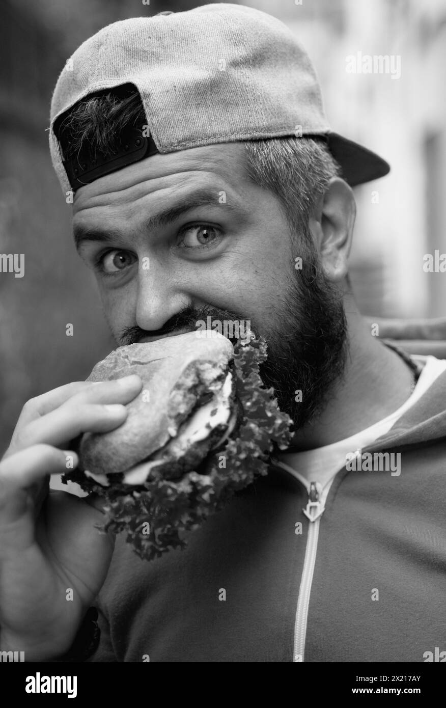 Hunger Man mangia hamburger all'aperto. L'uomo mangia gustosi hamburger per strada. Burger a pranzo. Cheeseburger o hamburger. Uomo che mangia gustosi hamburger all'aperto Foto Stock