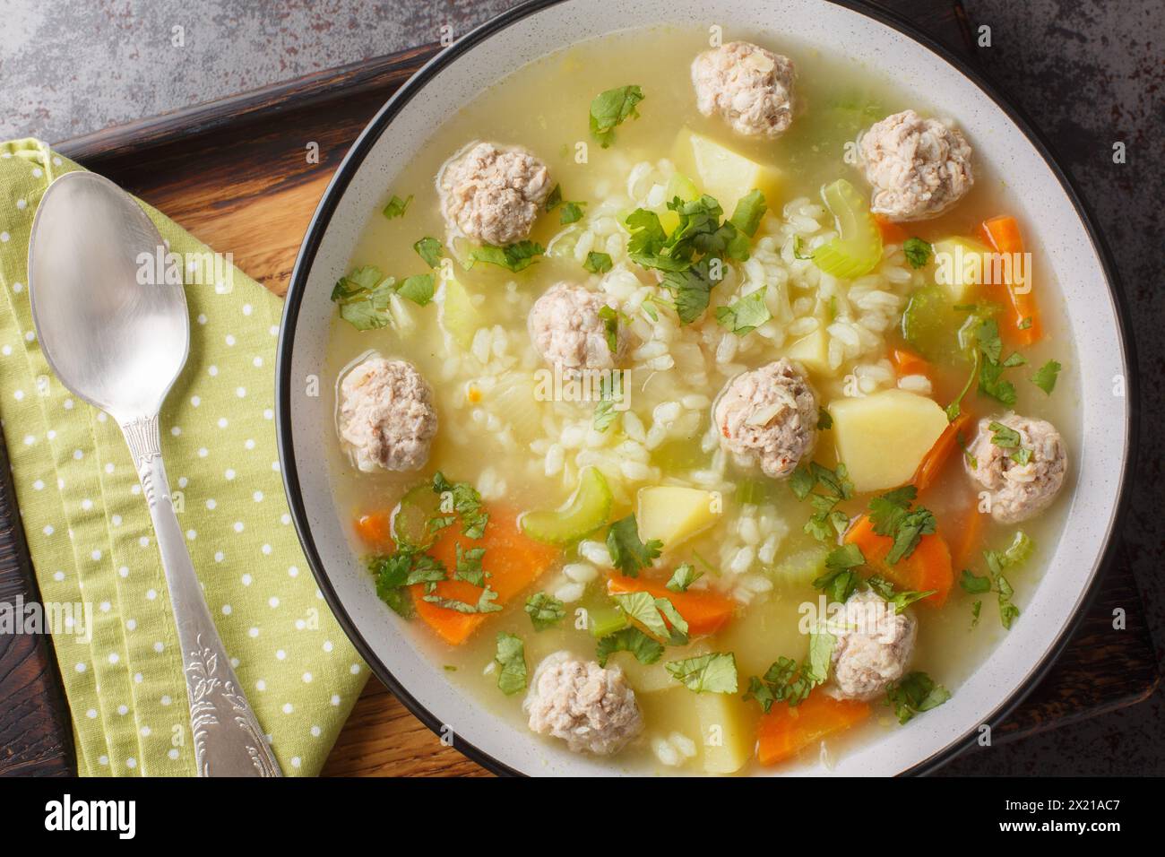 Zuppa calda di polpette di riso fatta in casa con sedano, carote, cipolle e patate da vicino in un recipiente sul tavolo. Vista dall'alto orizzontale Foto Stock