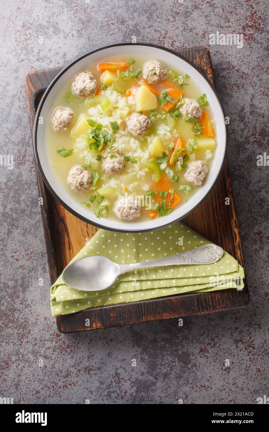 Zuppa di riso con polpette di sedano, carote, cipolle e patate da vicino in un recipiente sul tavolo. Vista dall'alto verticale Foto Stock