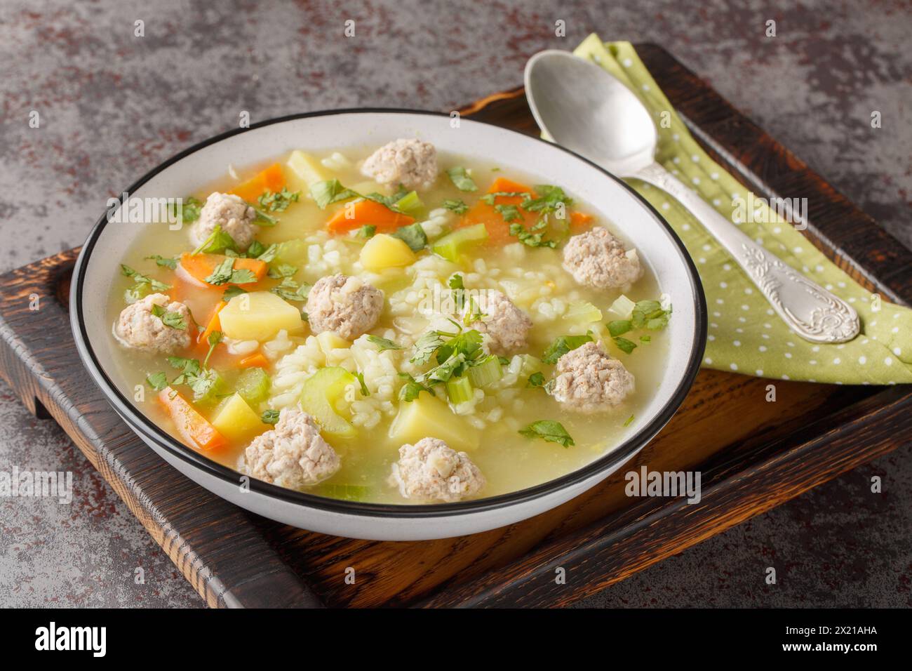 Zuppa dietetica di polpette di riso con sedano, carote, cipolle, patate ed erbe aromatiche da vicino in un recipiente sul tavolo. Orizzontale Foto Stock