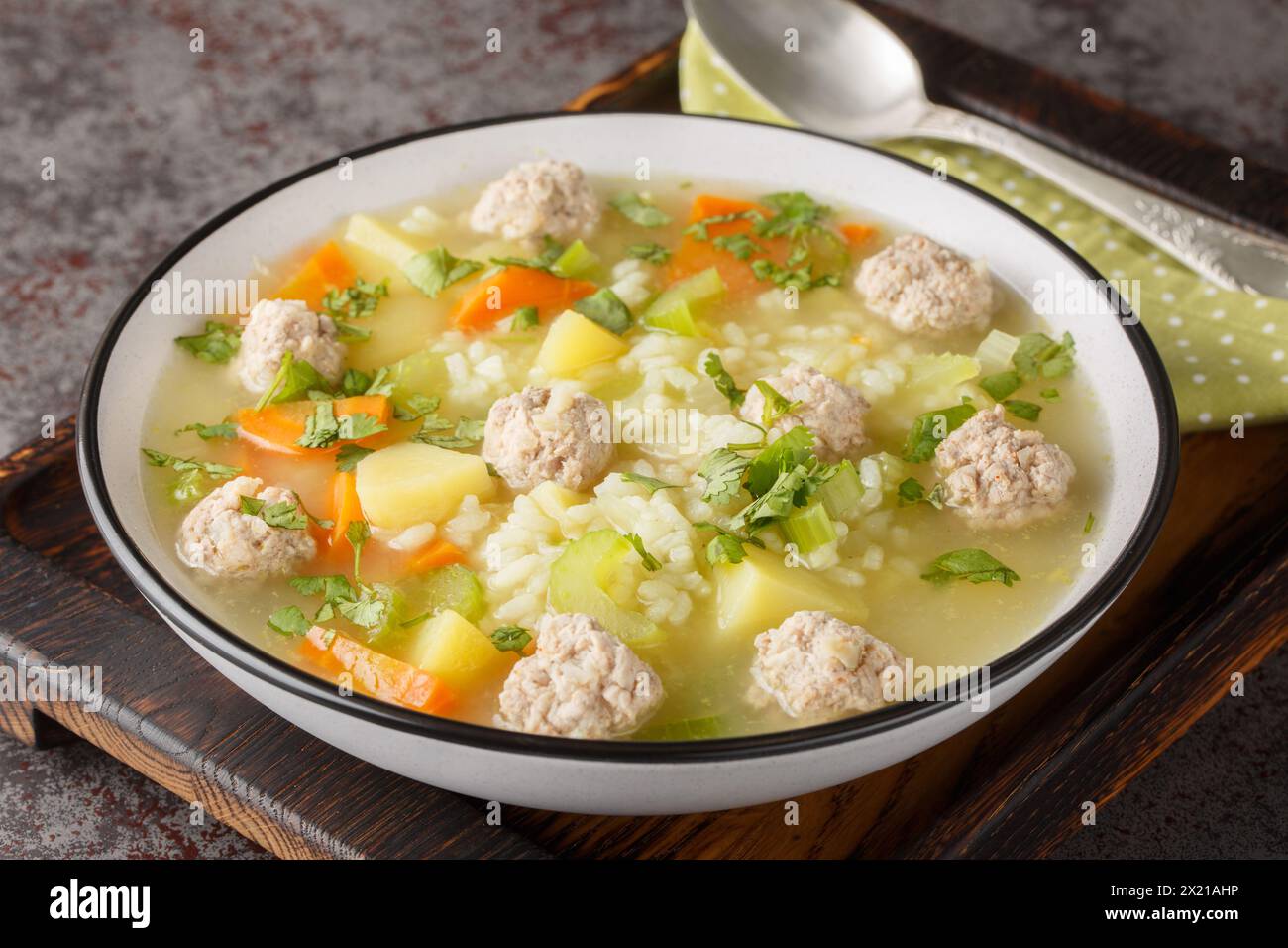 Zuppa calda di polpette di riso fatta in casa con sedano, carote, cipolle e patate da vicino in un recipiente sul tavolo. Orizzontale Foto Stock