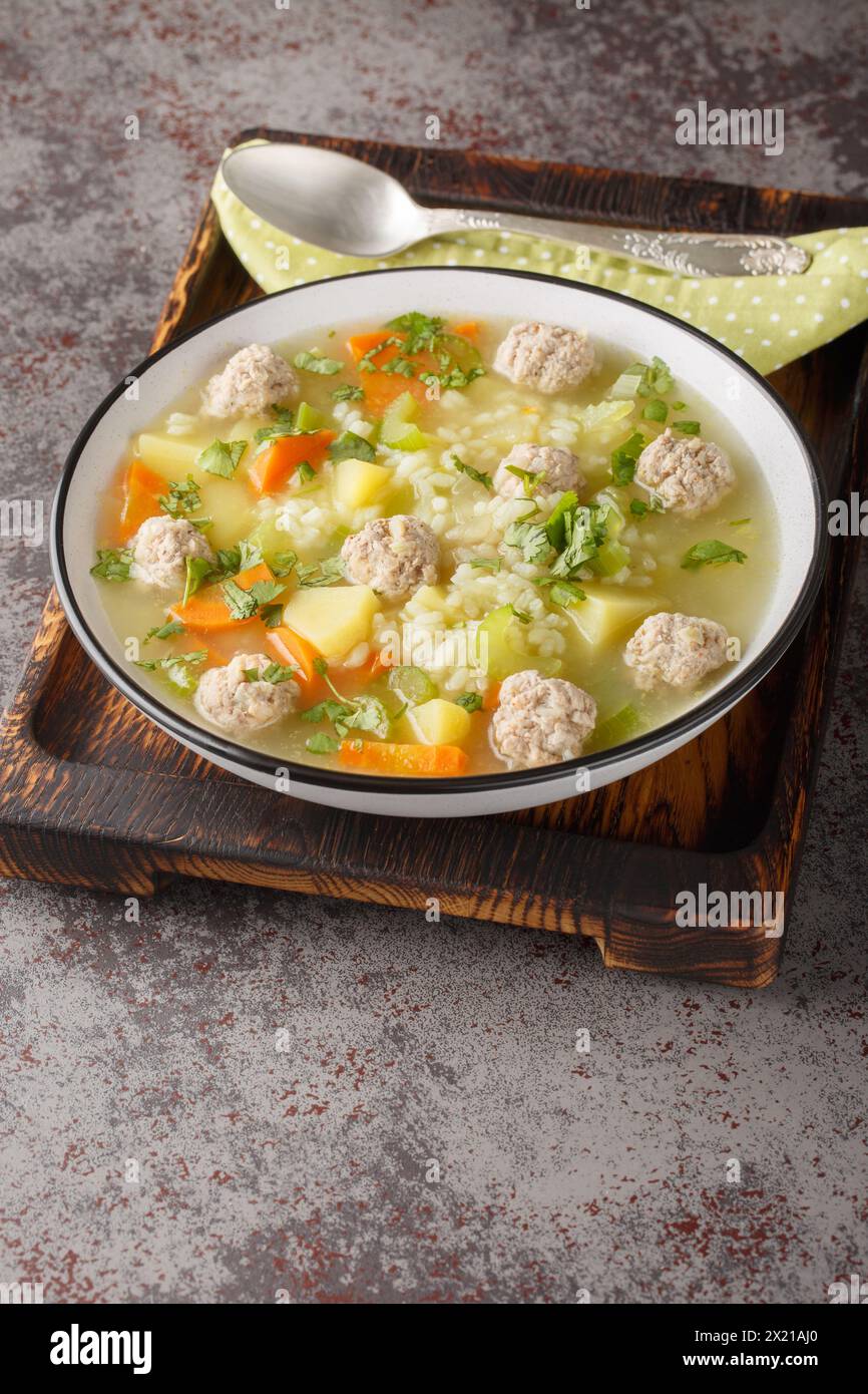 Zuppa di riso con polpette di sedano, carote, cipolle e patate da vicino in un recipiente sul tavolo. Verticale Foto Stock