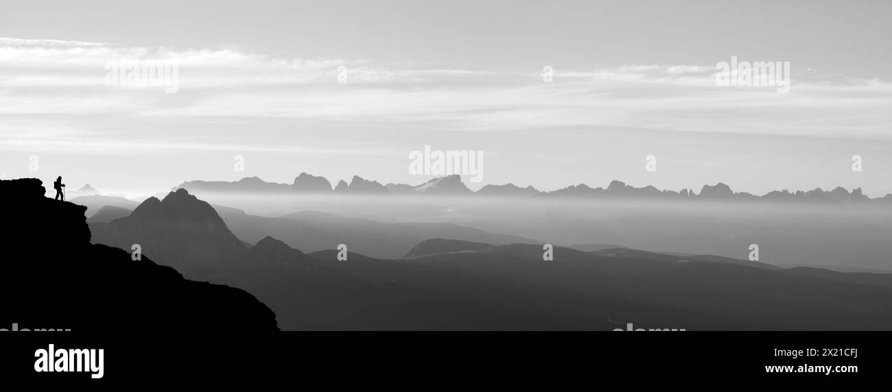 Panorama con la donna su una sporgenza rocciosa e vista in lontananza delle Dolomiti con Peitlerkofel, Iffinger Spitze, Sella, Langkofel, Plattkofel, Marmolada, Rosengario Foto Stock