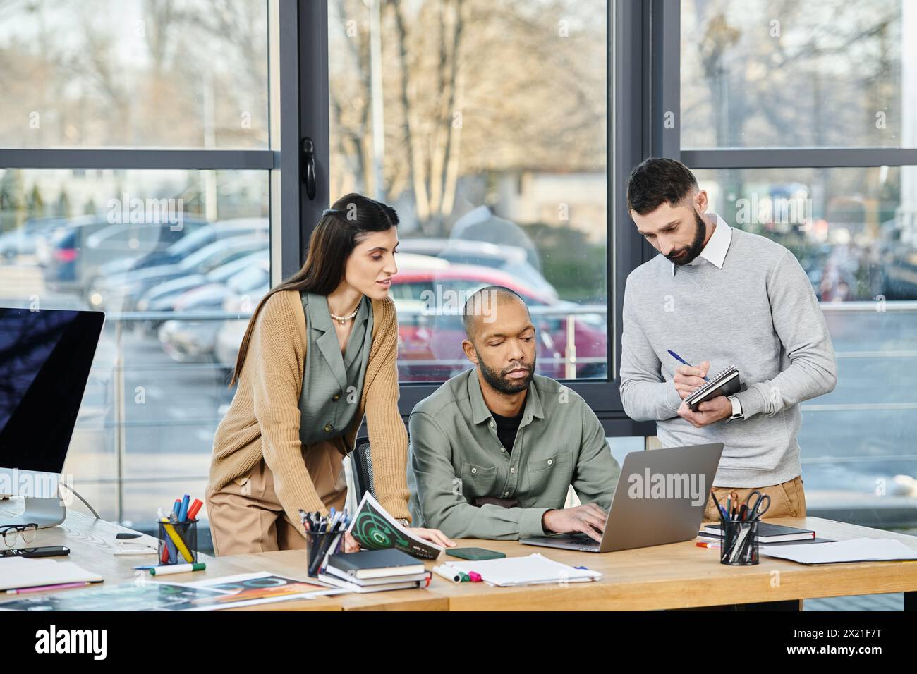 Tre professionisti aziendali si impegnano in una discussione di progetto su un notebook in un ambiente aziendale, diversità e inclusione Foto Stock