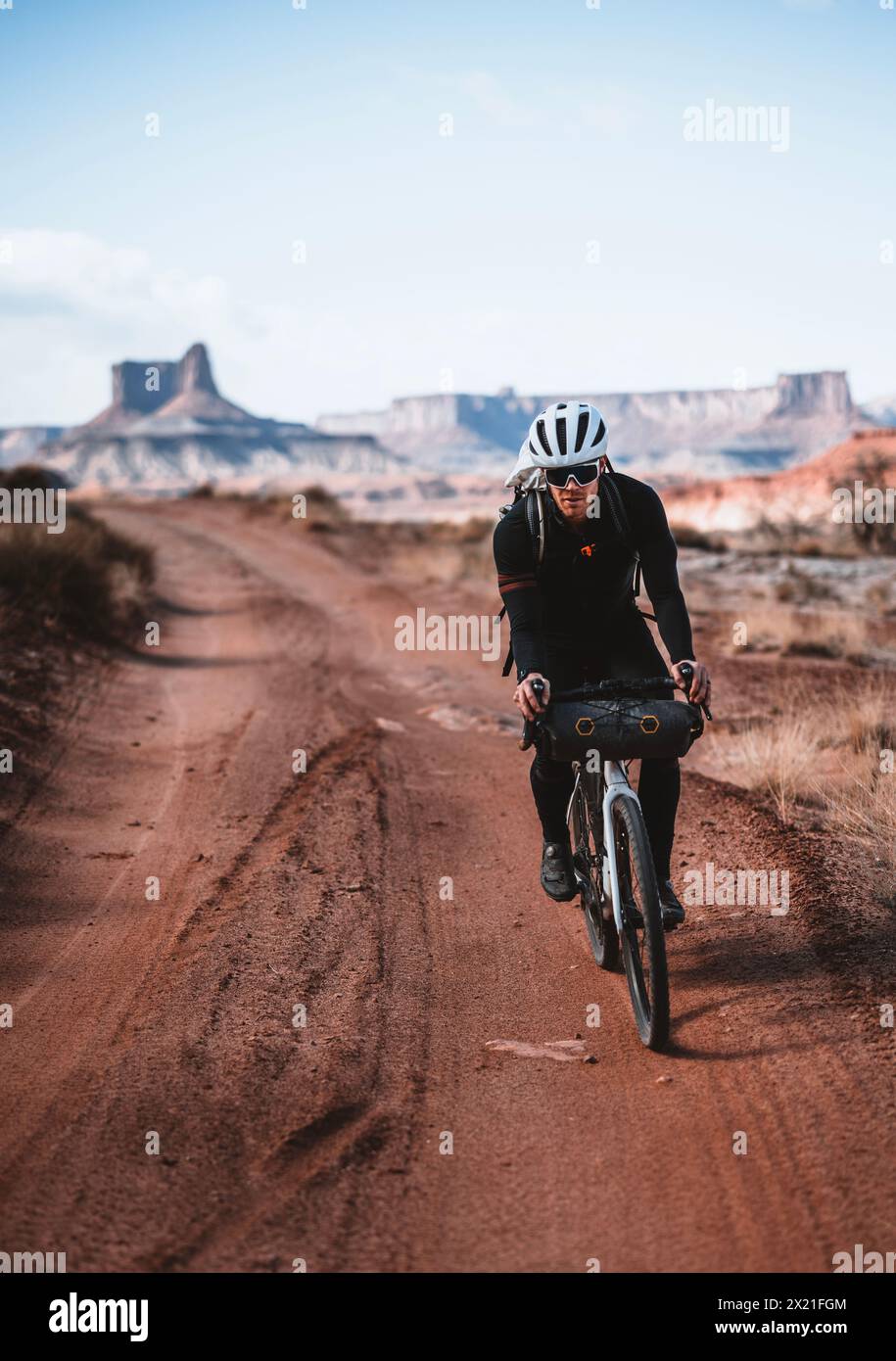 Un ciclista maschile corre lungo la remota strada desertica a Canyonlands, Utah Foto Stock