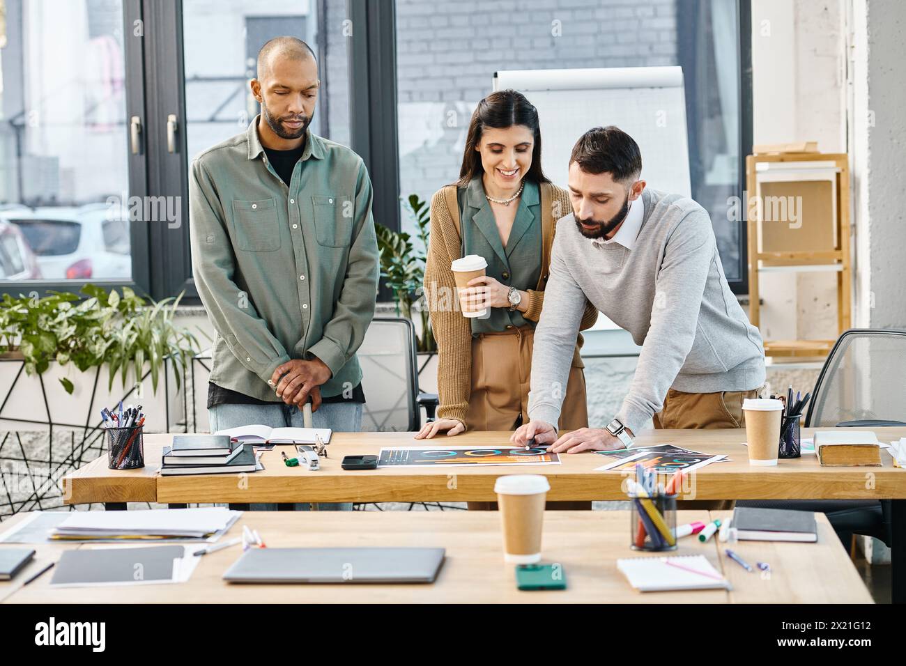 Un gruppo eterogeneo di persone in abbigliamento da lavoro si trova intorno a un tavolo di legno, impegnato in una discussione di progetto. Foto Stock