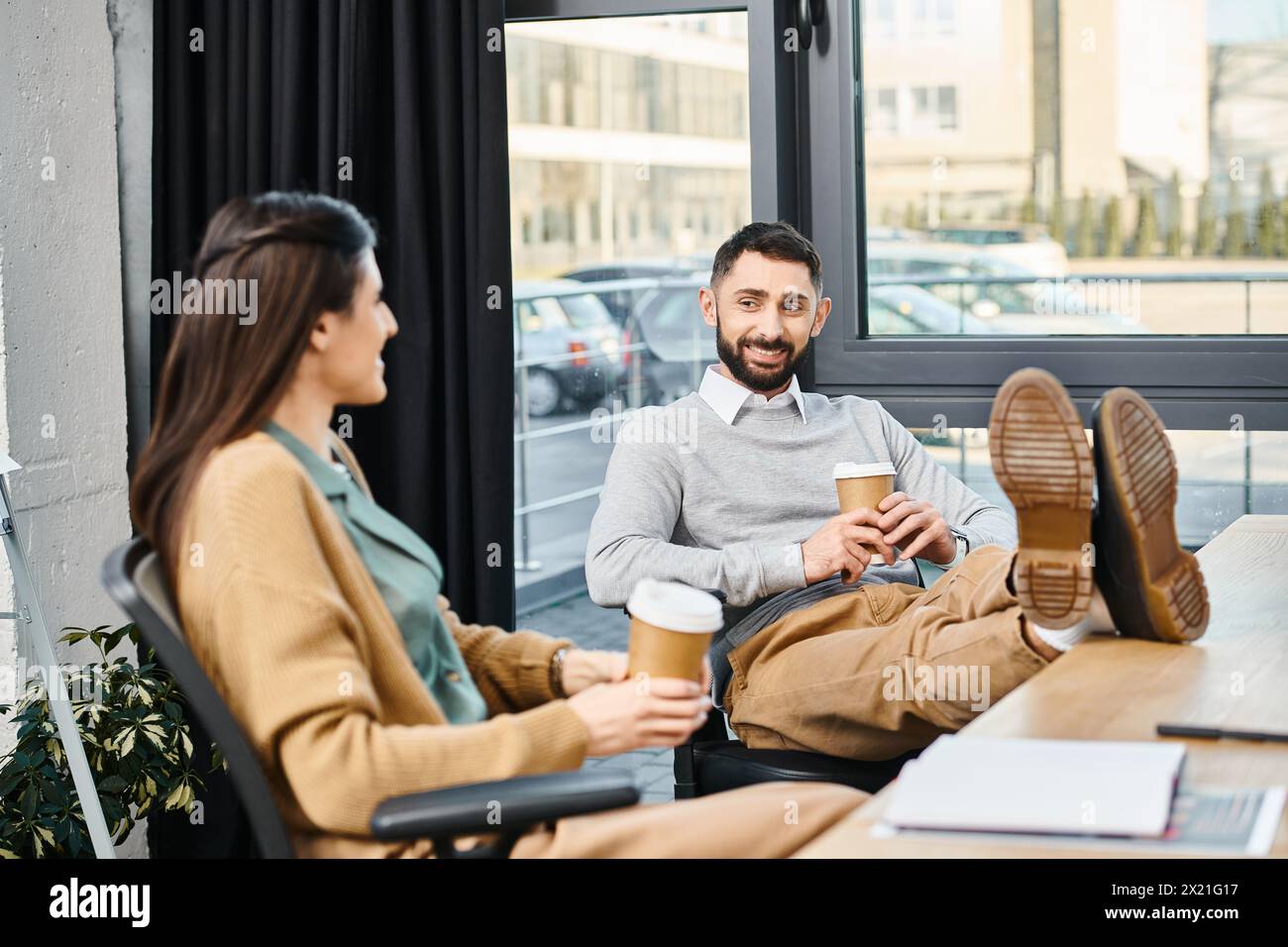 Una coppia gode di un momento tranquillo insieme a un tavolo, assaporando tazze di caffè in un ambiente tranquillo da ufficio. Foto Stock