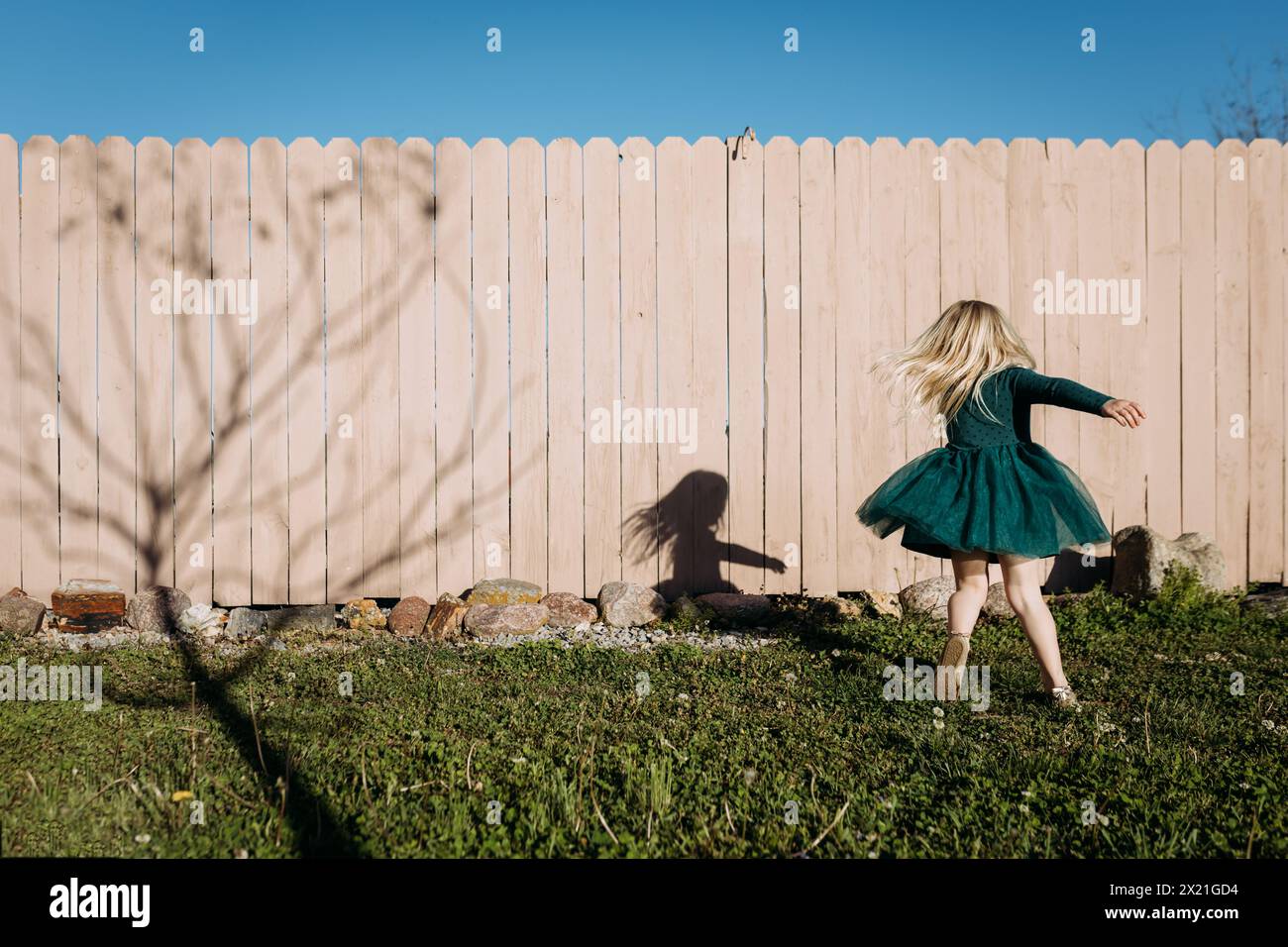 Giovane ragazza che si avvolge in abito in giardino in una vivace giornata di sole Foto Stock