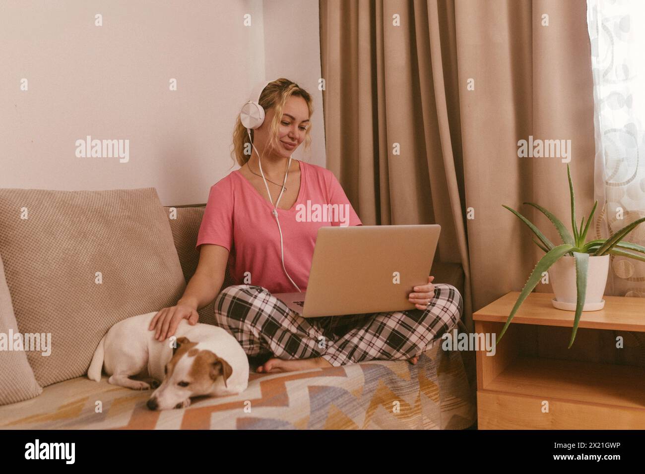 Una ragazza con un cane che guarda un film su un computer portatile dotato di cuffie. Foto Stock
