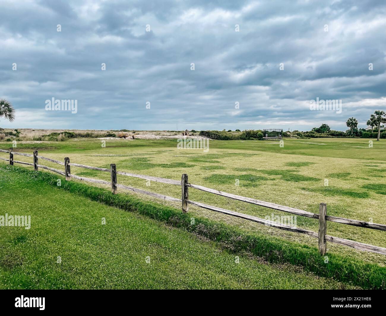 Vasto campo verde aperto con recinzione rustica in legno in una giornata nuvolosa Foto Stock
