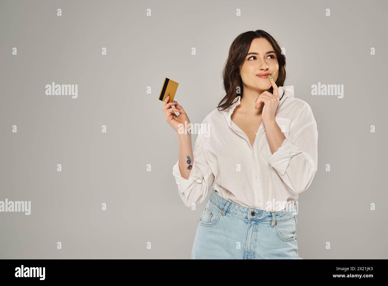La camicia bianca Plus size trasuda eleganza mentre reggi una carta oro su uno sfondo grigio. Foto Stock