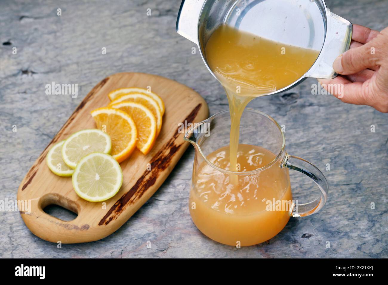 Tè freddo fatto in casa a base di tè alle erbe con succo di mela, succo d'arancia, menta d'acqua, maggiorana selvatica, fase 2: Il succo d'arancia viene versato nel succo di mela, Foto Stock