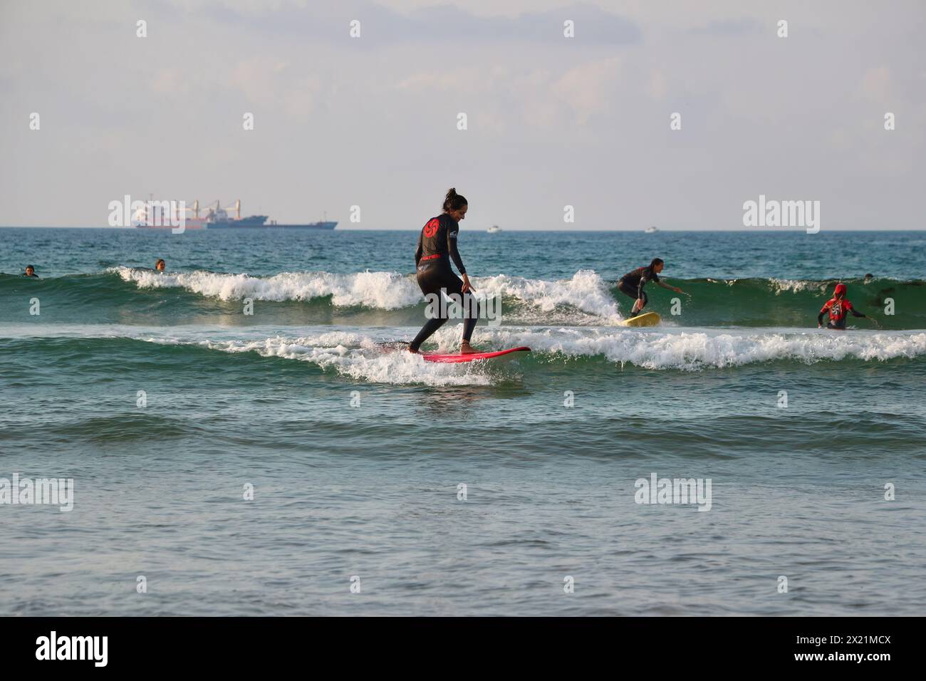 Surfisti durante una lezione con piccole onde e navi da carico ancorate lontane all'orizzonte Somo Ribamontán al Mar Cantabria Spagna Foto Stock