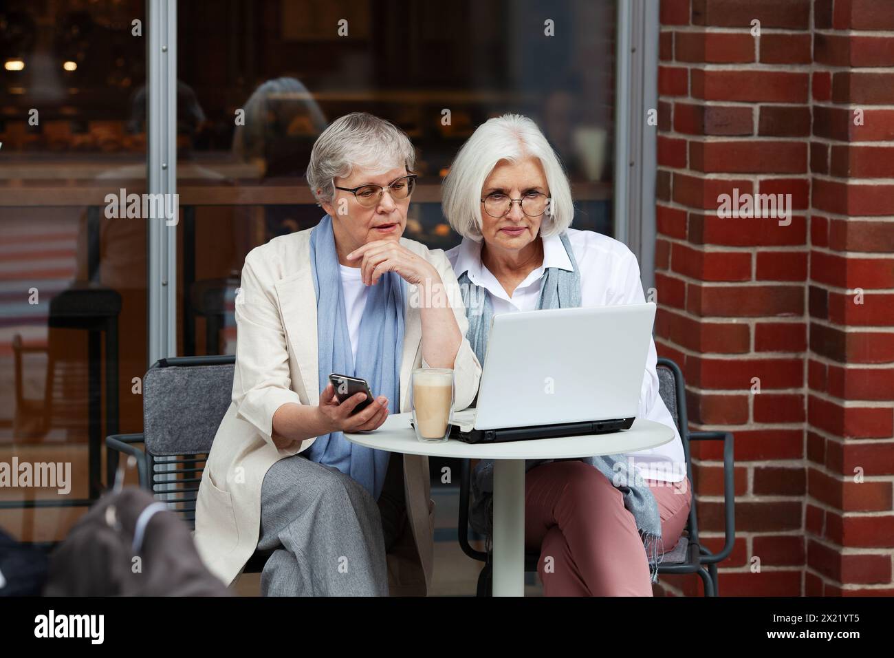 Donne d'affari mature alle riunioni d'affari si mettono al tavolo con un computer portatile nel caffè, trasudando professionalità e imprenditorialità. Bella modalità anziani anziani Foto Stock