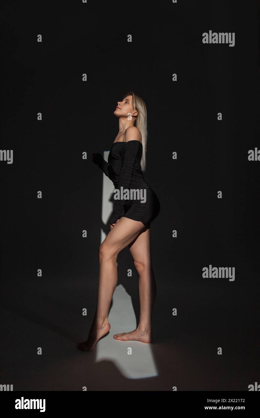 Elegante e bella giovane donna in Un abito sexy Fashion Black con gambe sottili al buio con luce Foto Stock