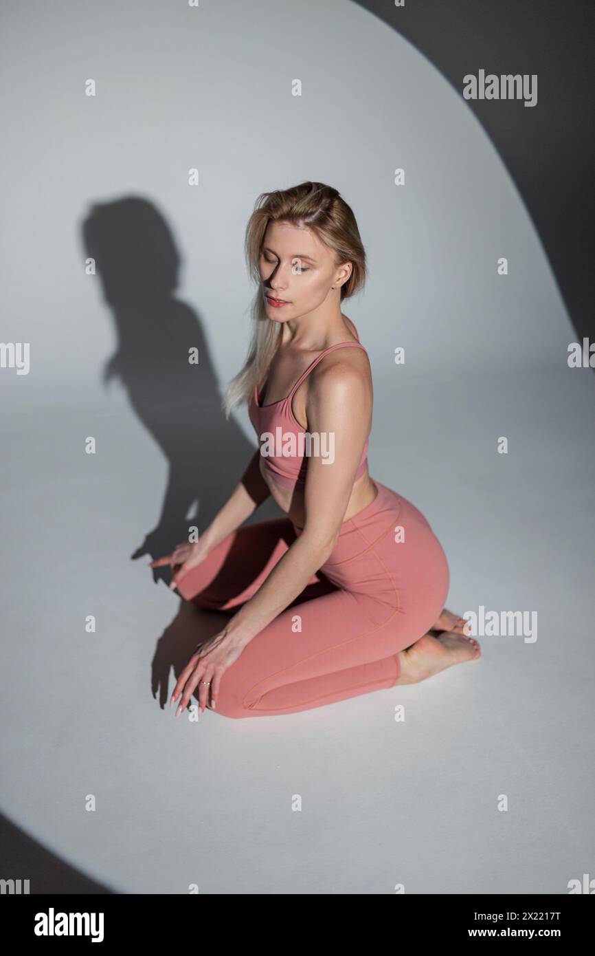 Bellissima yoga femminile atletica sottile in abbigliamento sportivo con Top e leggings si siede e posa nello studio Foto Stock