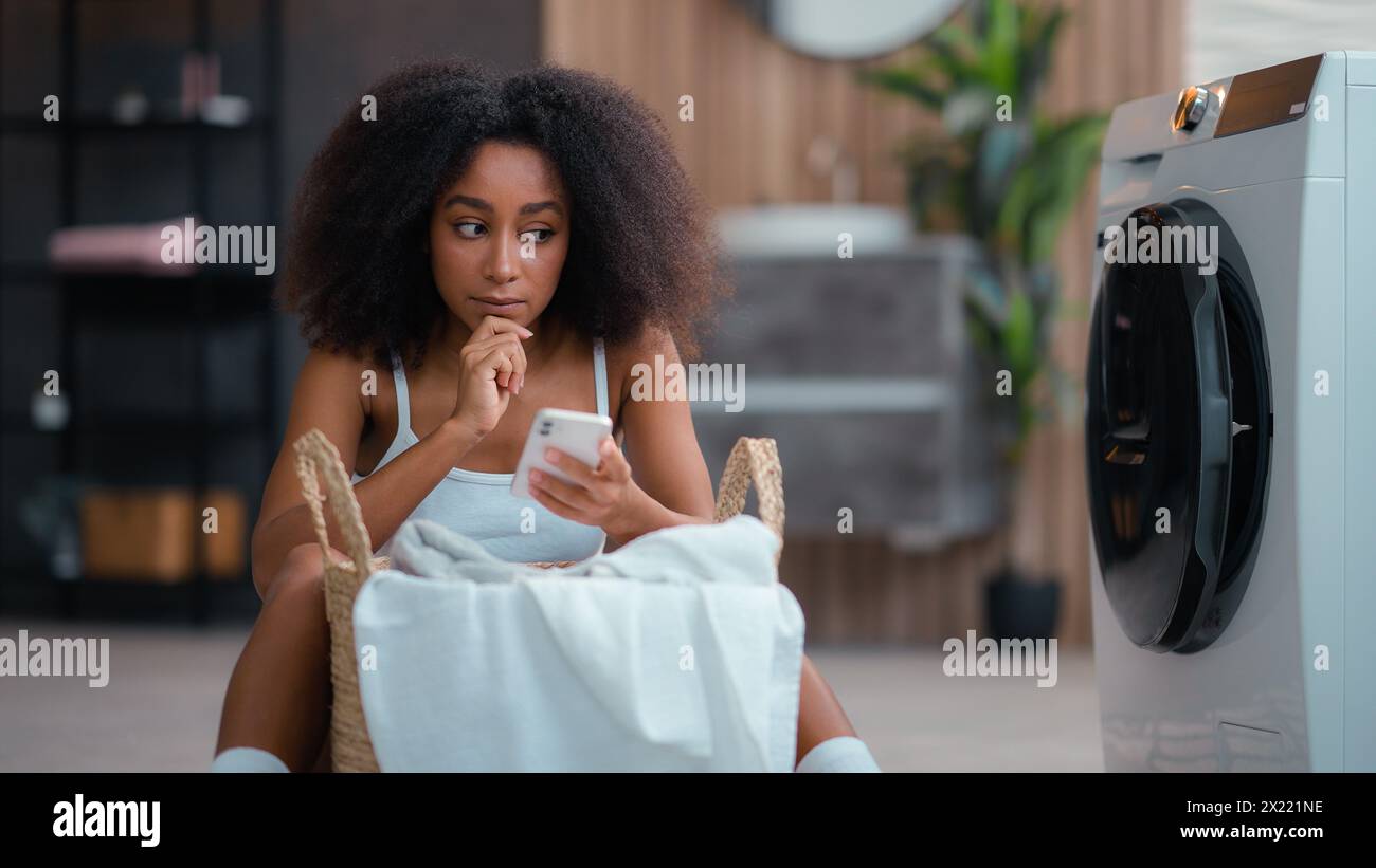 Donna afro-americana ragazza pensante pensante pensante pensiero pensante soluzione pensata esitare decidere utilizzando il telefono cellulare online shopping Foto Stock