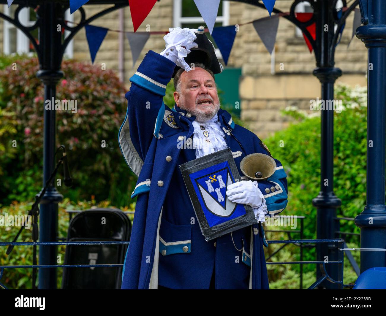 Uomo pigrillo e fattorino (livrea e vestiti blu) che fanno annunci e annunci pubblici rumorosi - Ilkley, West Yorkshire, Inghilterra, Regno Unito. Foto Stock