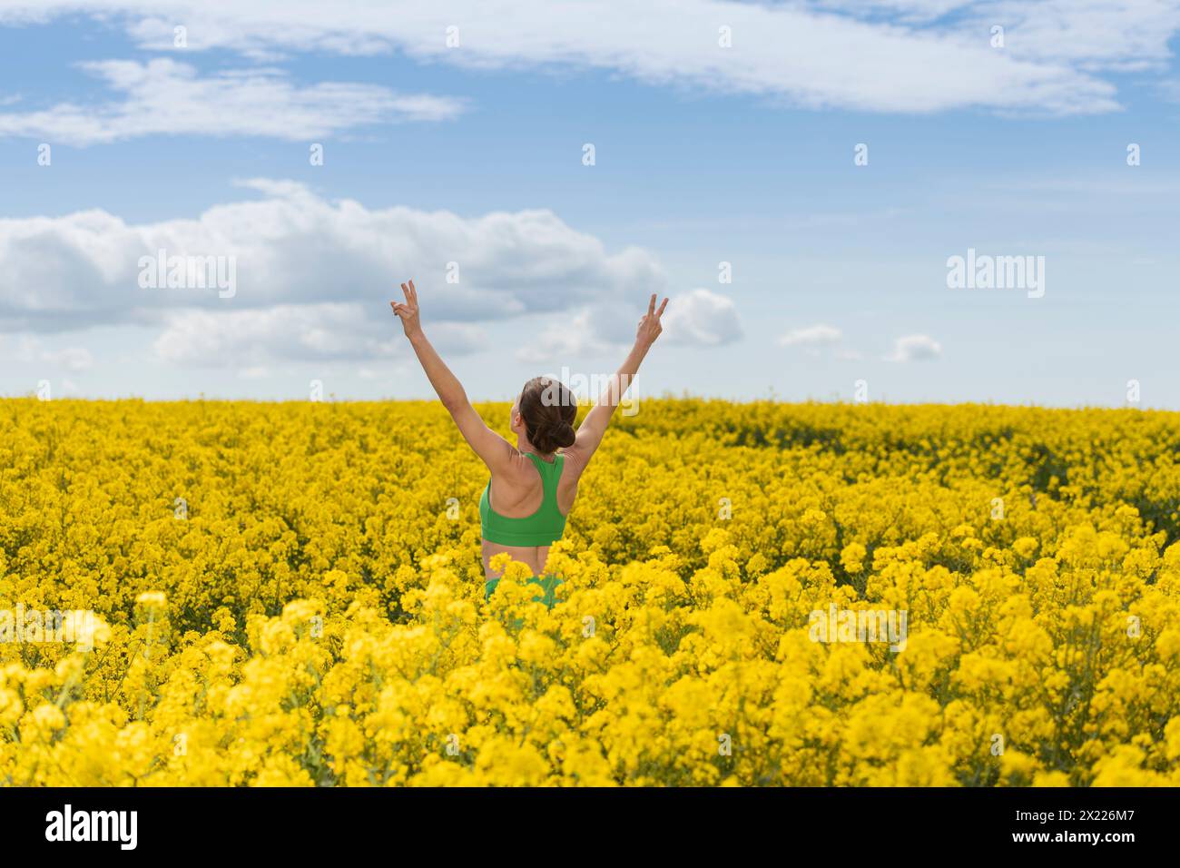 Donna sportiva con le braccia alzate per festeggiare e godersi il sole in un campo di colza giallo Foto Stock