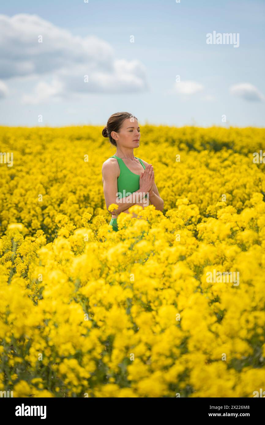 Donna che meditava in un campo di colza giallo, in primavera. elimina lo stress dalla vita di tutti i giorni Foto Stock