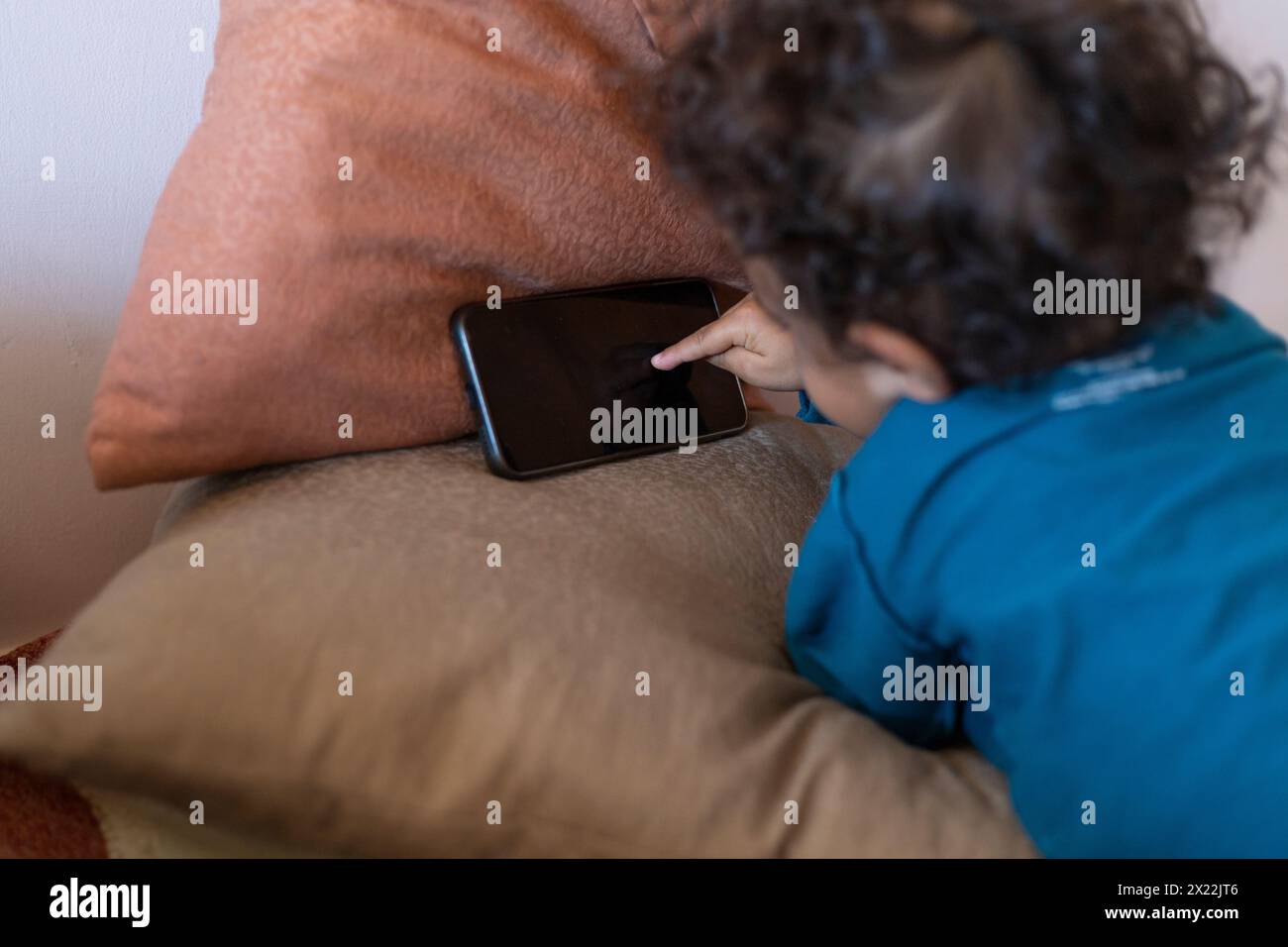 Il ragazzo latino-americano (2) tocca lo schermo del telefono cellulare di sua madre in cerca dei suoi video dei cartoni animati. Concetto tecnologico per bambini Foto Stock