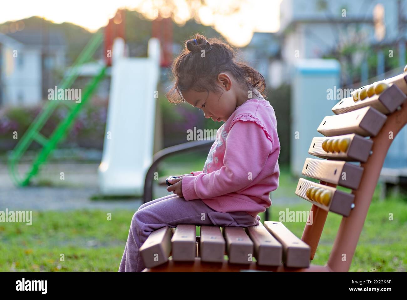 Un bambino che utilizza o gioca con uno smartphone al parco giochi invece di giocare. Una bambina che guarda video su uno smartphone. Foto Stock