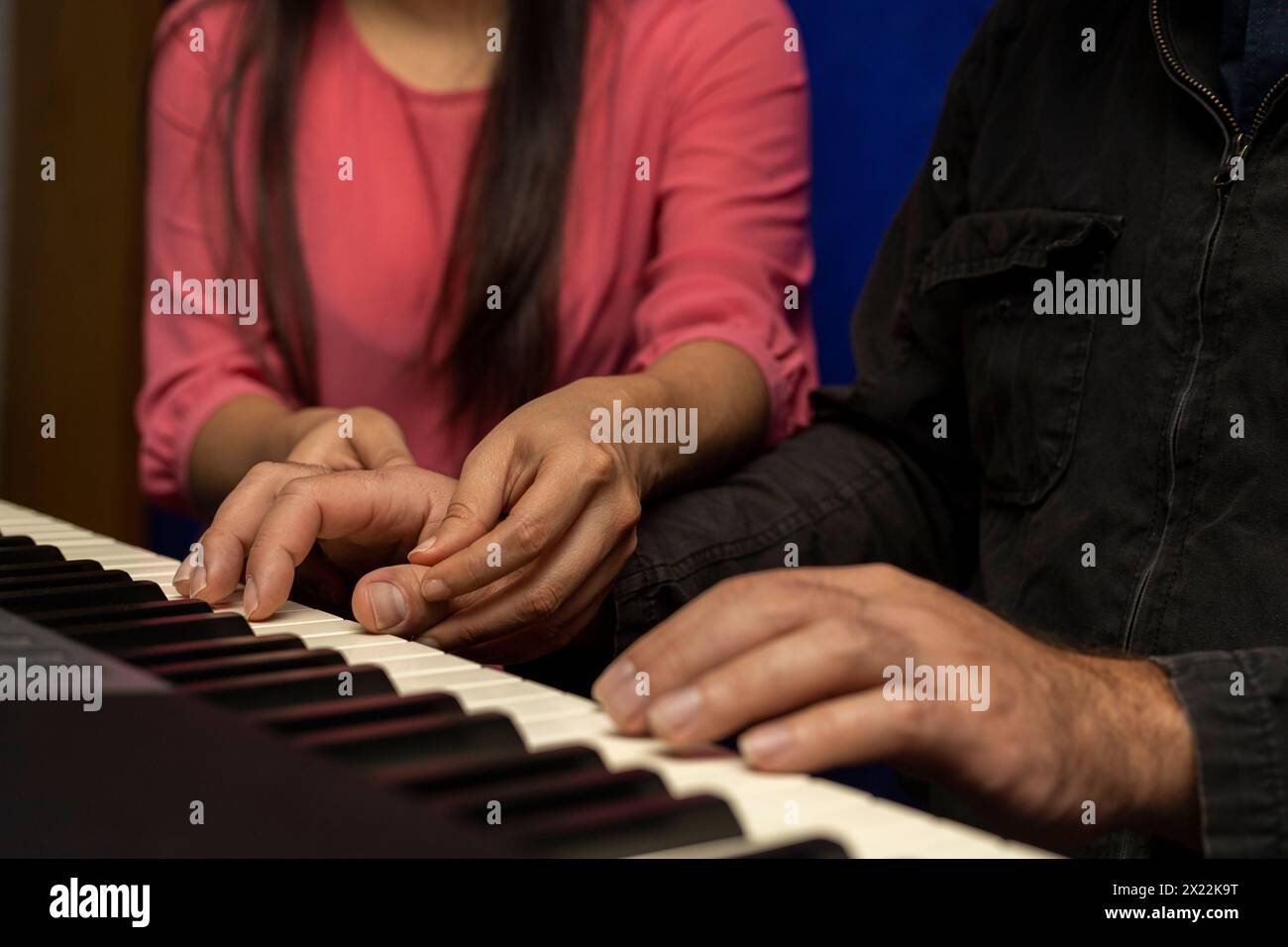 Un insegnante latinoamericano irriconoscibile insegna e corregge la postura per suonare la tastiera del pianoforte. Concetto di lezioni di musica Foto Stock