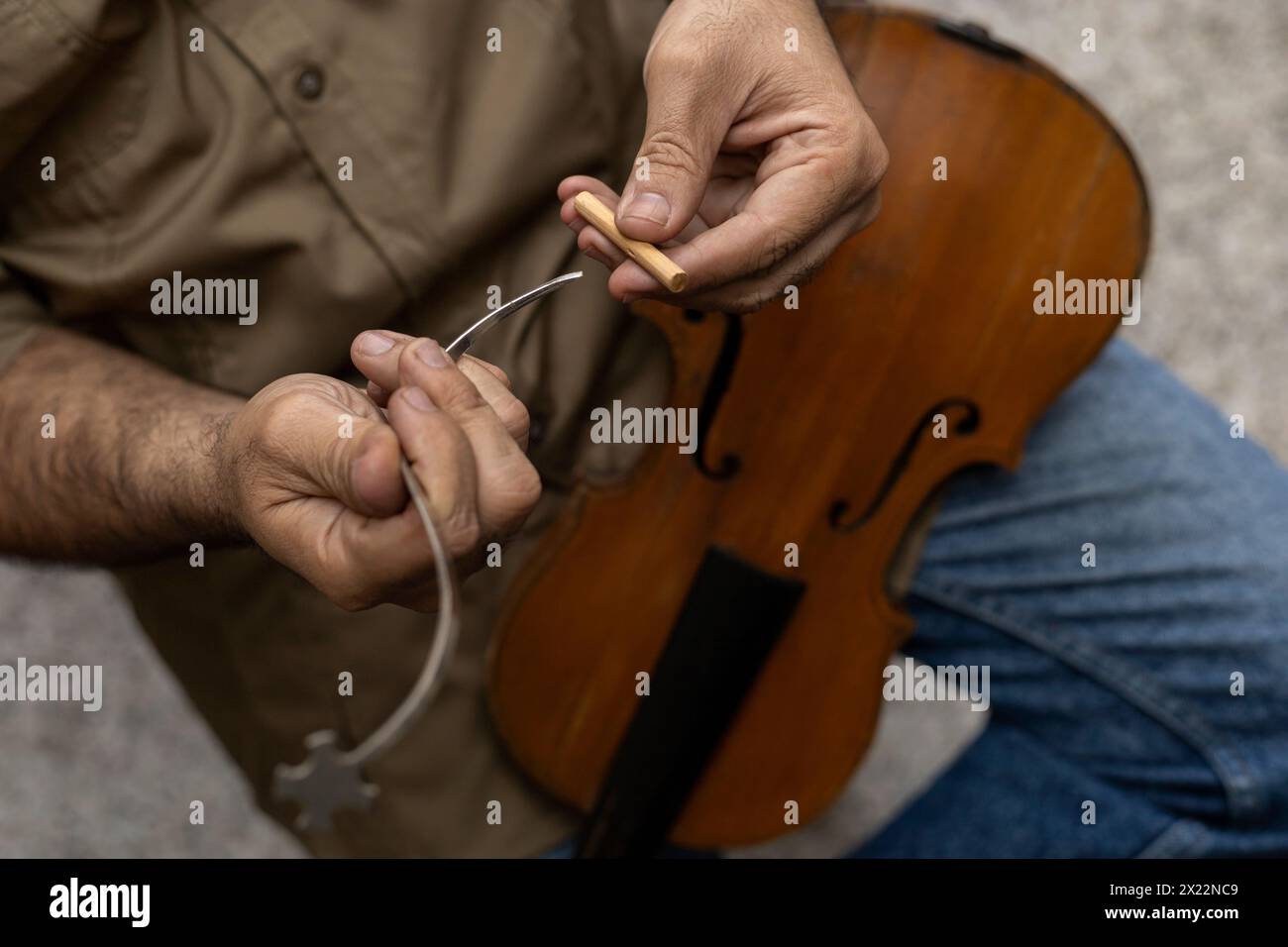 Vista dall'alto di un liutaio latinoamericano che colloca in un attrezzo speciale un palo sonoro posizionato all'interno dello strumento dalla pressione tra la parte superiore e la b Foto Stock