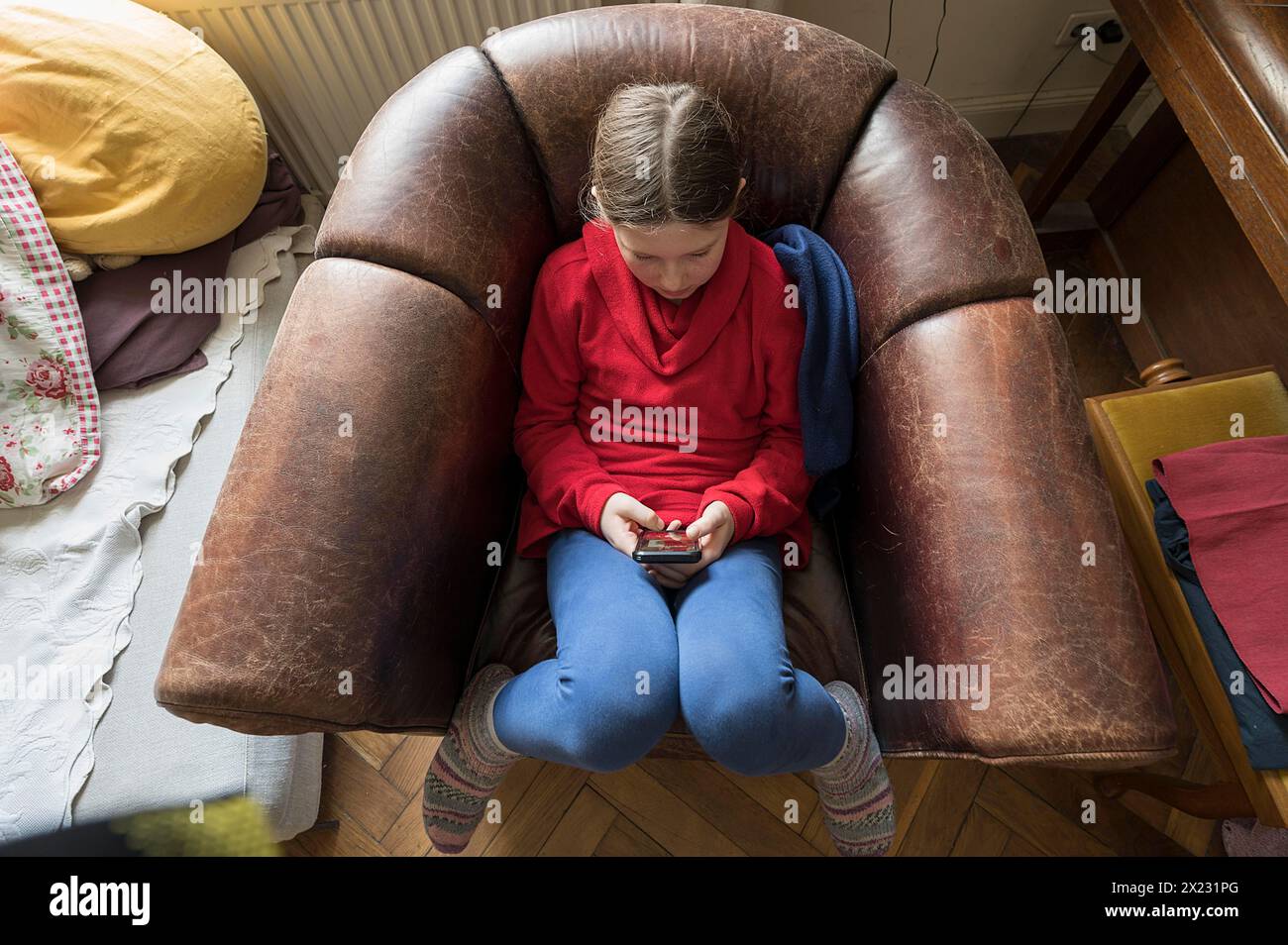 Symbol foto telefono cellulare, Internet, dipendenza, bambina, 10 anni, seduta su una poltrona con il suo telefono cellulare, Mecklenurg-Vorpommern Foto Stock