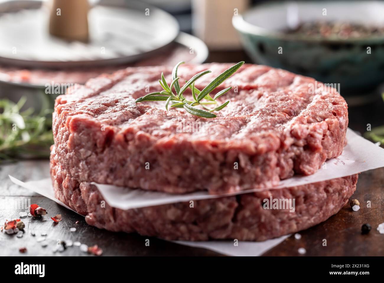 Polpette di manzo crude fresche con sale al rosmarino e pepe preparate in forma di carne su un tagliere. Foto Stock