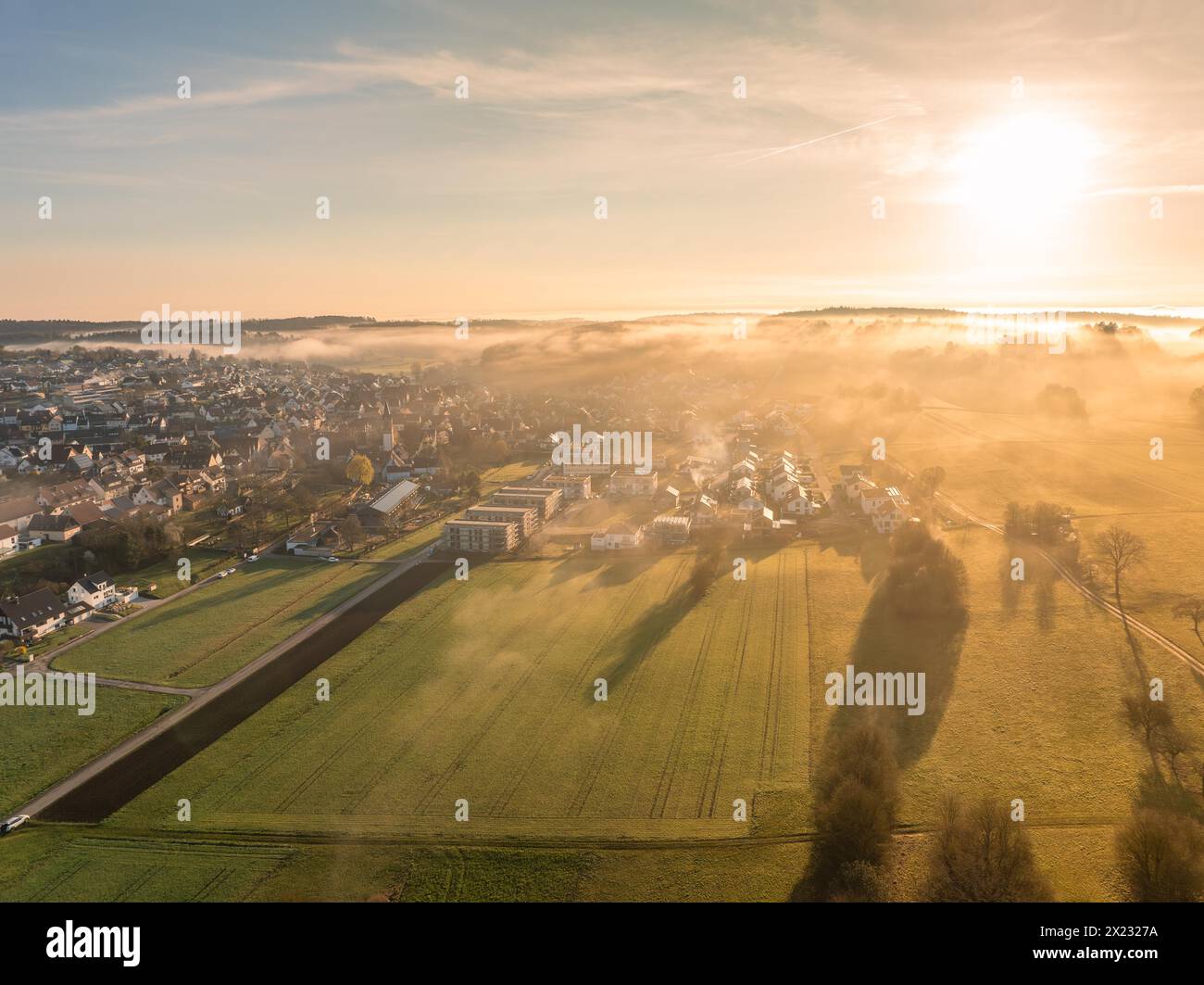 Alba dietro una piccola città con nebbia sui campi in primo piano, Gechingen, Foresta Nera, Germania Foto Stock