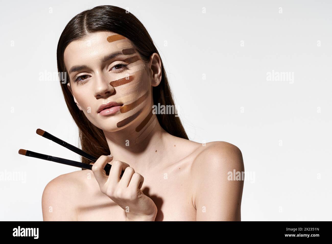 Donna graziosa con vari pennelli per il trucco sul viso, creando un look creativo e artistico con fondazioni. Foto Stock