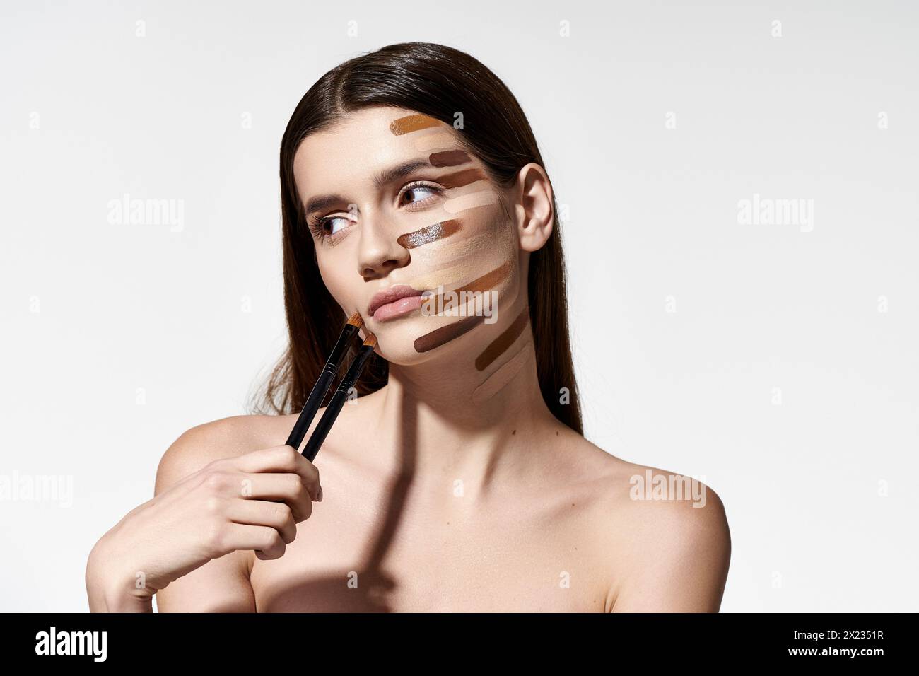 Donna di gusto con vari pennelli per il trucco sul viso, creando un look creativo e artistico con fondazioni. Foto Stock