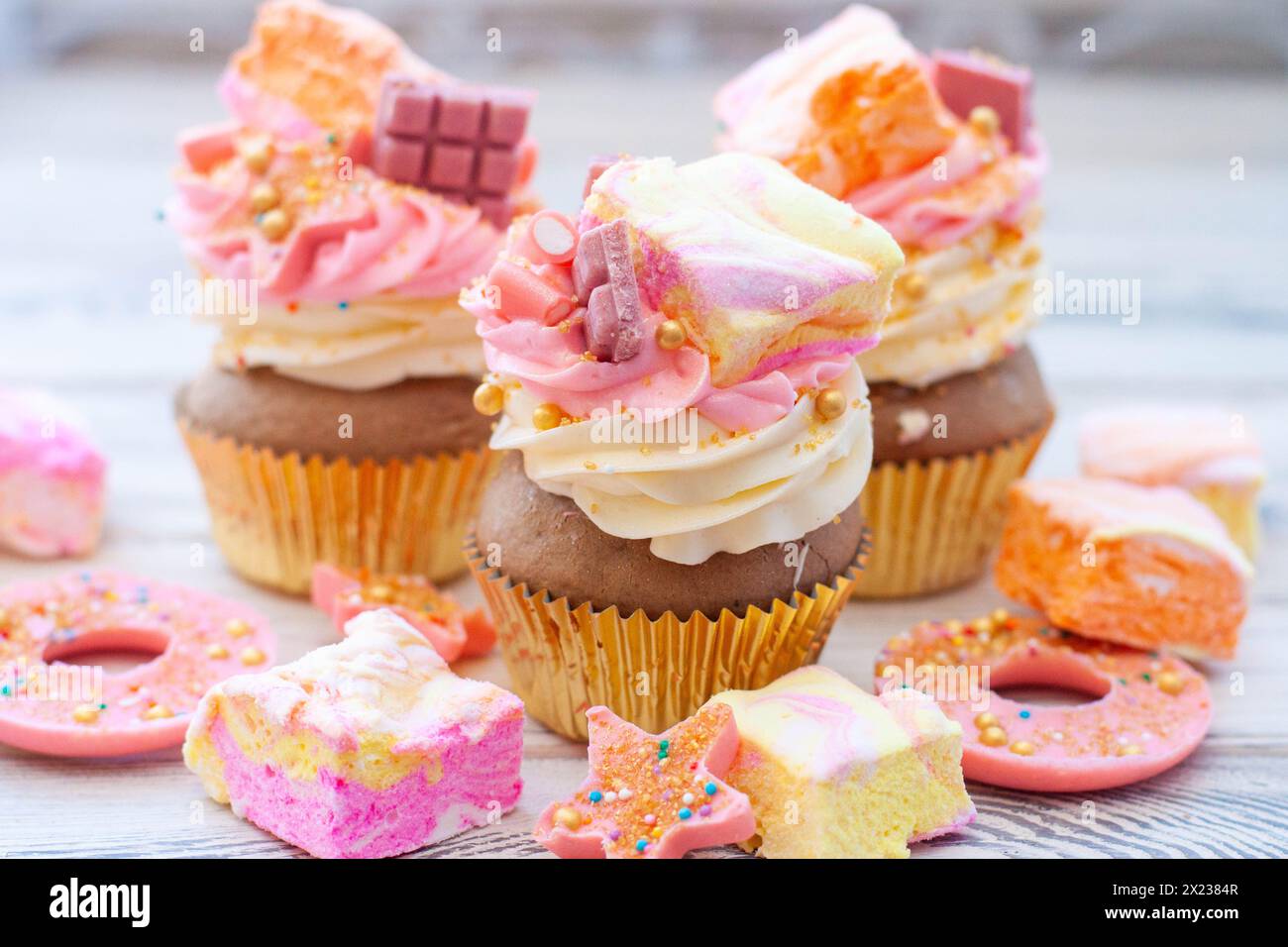 Cupcake rosa color pastello con cioccolato, ciambelle e marshmallow arcobaleno Foto Stock