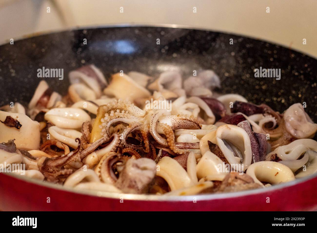 Concediti il brivido e l'aroma della frittura di calamari appena cucinata nella padella. Provate l'arte culinaria e la delizia della cucina mediterranea Foto Stock