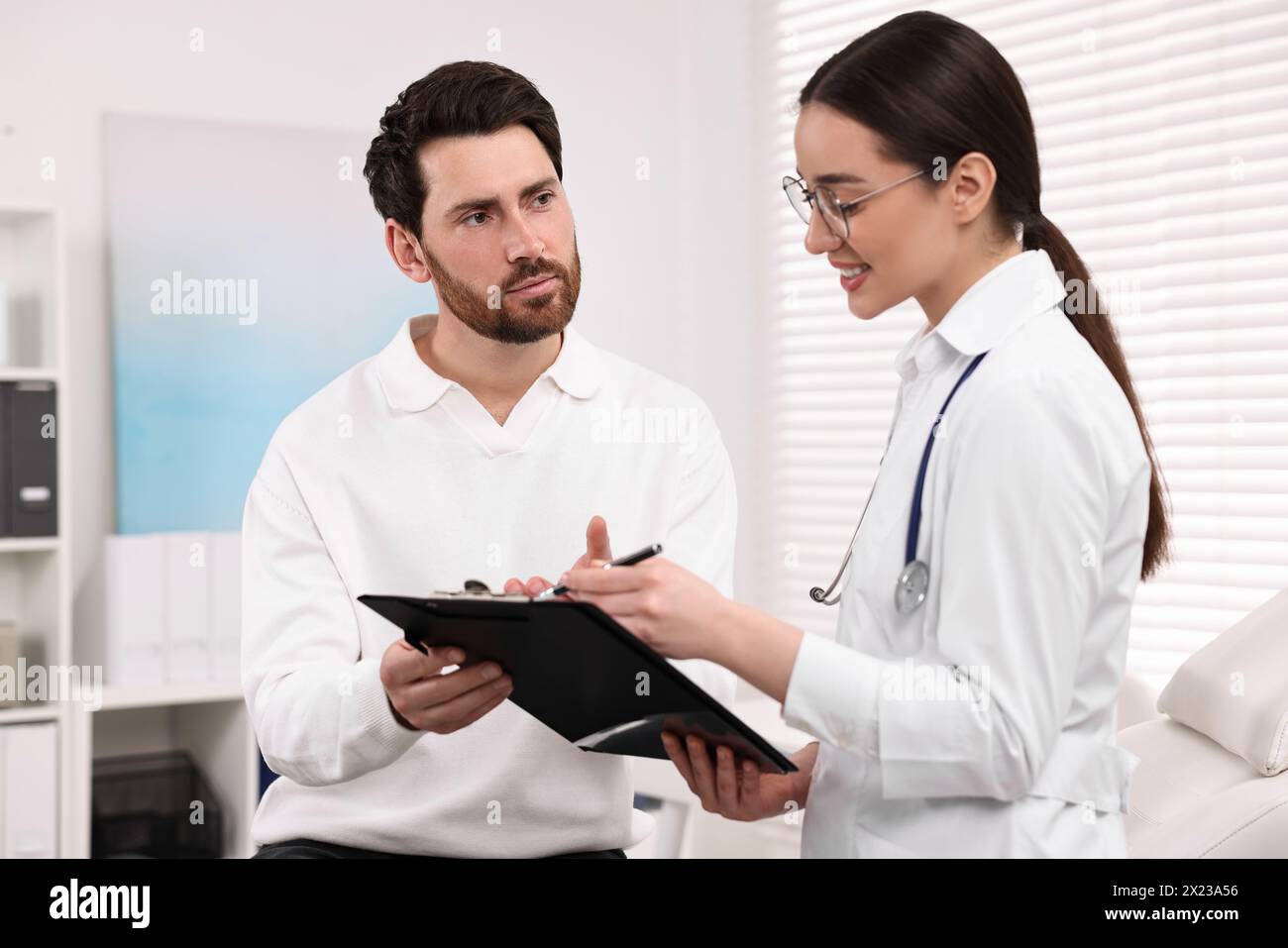 Medico con appunti che consulta il paziente durante l'appuntamento in clinica Foto Stock