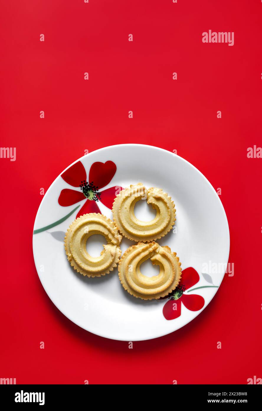 La vaniglia viennese mescola i biscotti su piatto bianco con motivo floreale rosso, presi su sfondo rosso Foto Stock