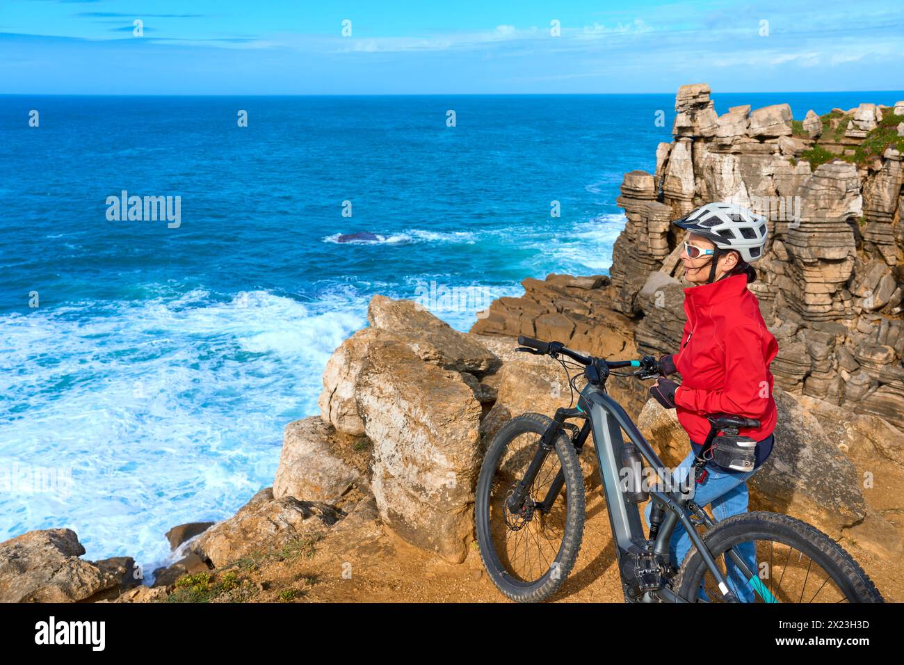 Coraggiosa donna anziana in sella alla sua mountain bike elettrica sulle scogliere rocciose di Peniche, sulla costa atlantica occidentale del Portogallo Foto Stock