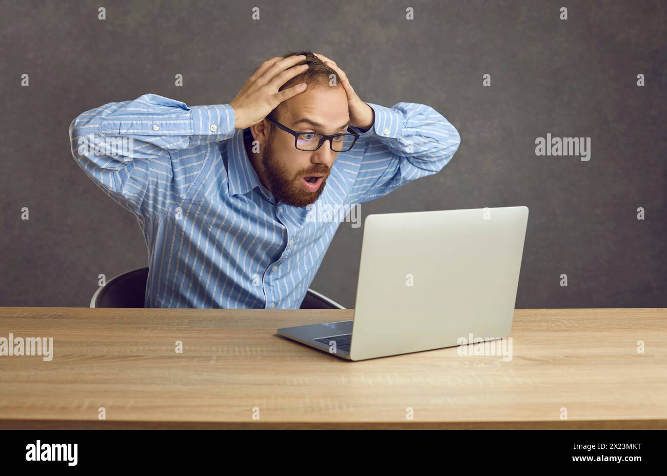 Un uomo scioccato frustrato e perplesso afferra la testa mentre guarda lo schermo del notebook. Foto Stock