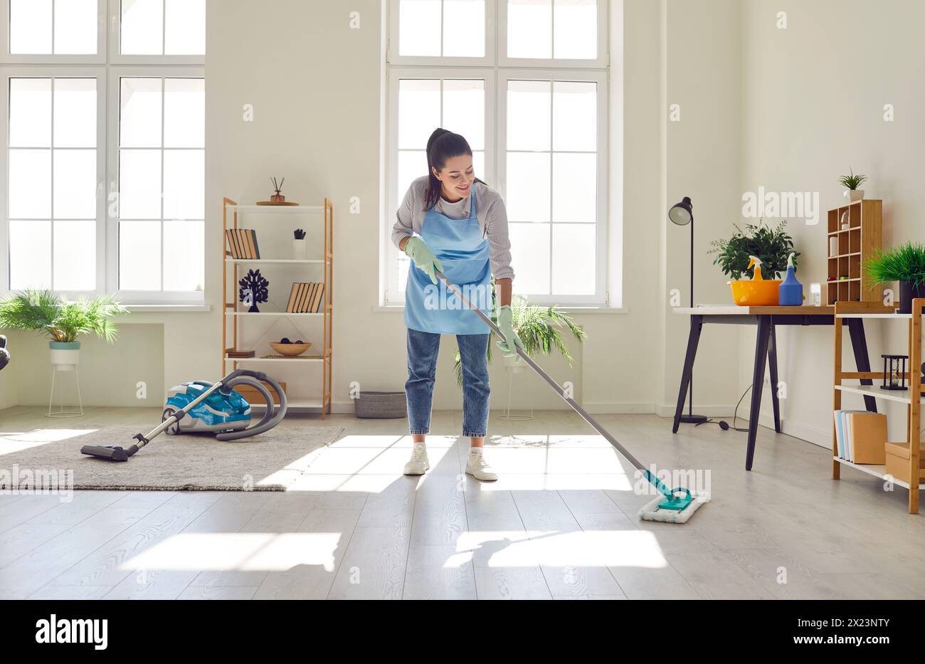 La giovane casalinga pulisce il pavimento con un panno per la pulizia a casa Foto Stock