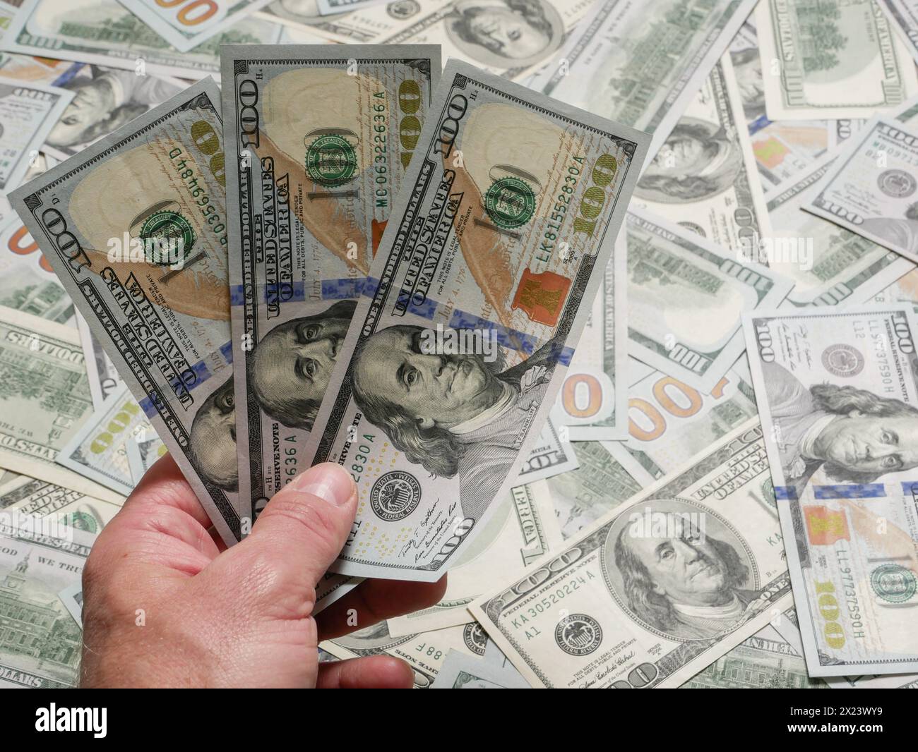 Mano umana in possesso di banconote da 100 dollari americani sullo sfondo di molte banconote da dollaro bugiardo. In possesso di banconote statunitensi, primo piano di mani.. Foto Stock