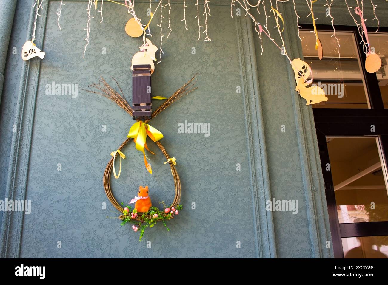 Decorazioni di Pasqua con giocattoli in legno intagliato e ghirlanda. Una corona di rami di salice stilizzati come un uovo pende sul muro di una casa. Vacanze di Pasqua. Foto Stock