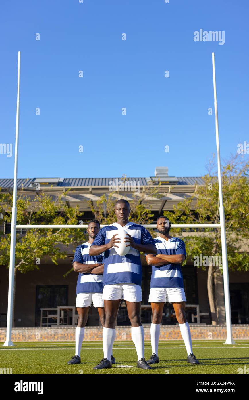 Tre giovani atleti afroamericani che tengono una palla da rugby sul campo all'aperto, spazio copia Foto Stock