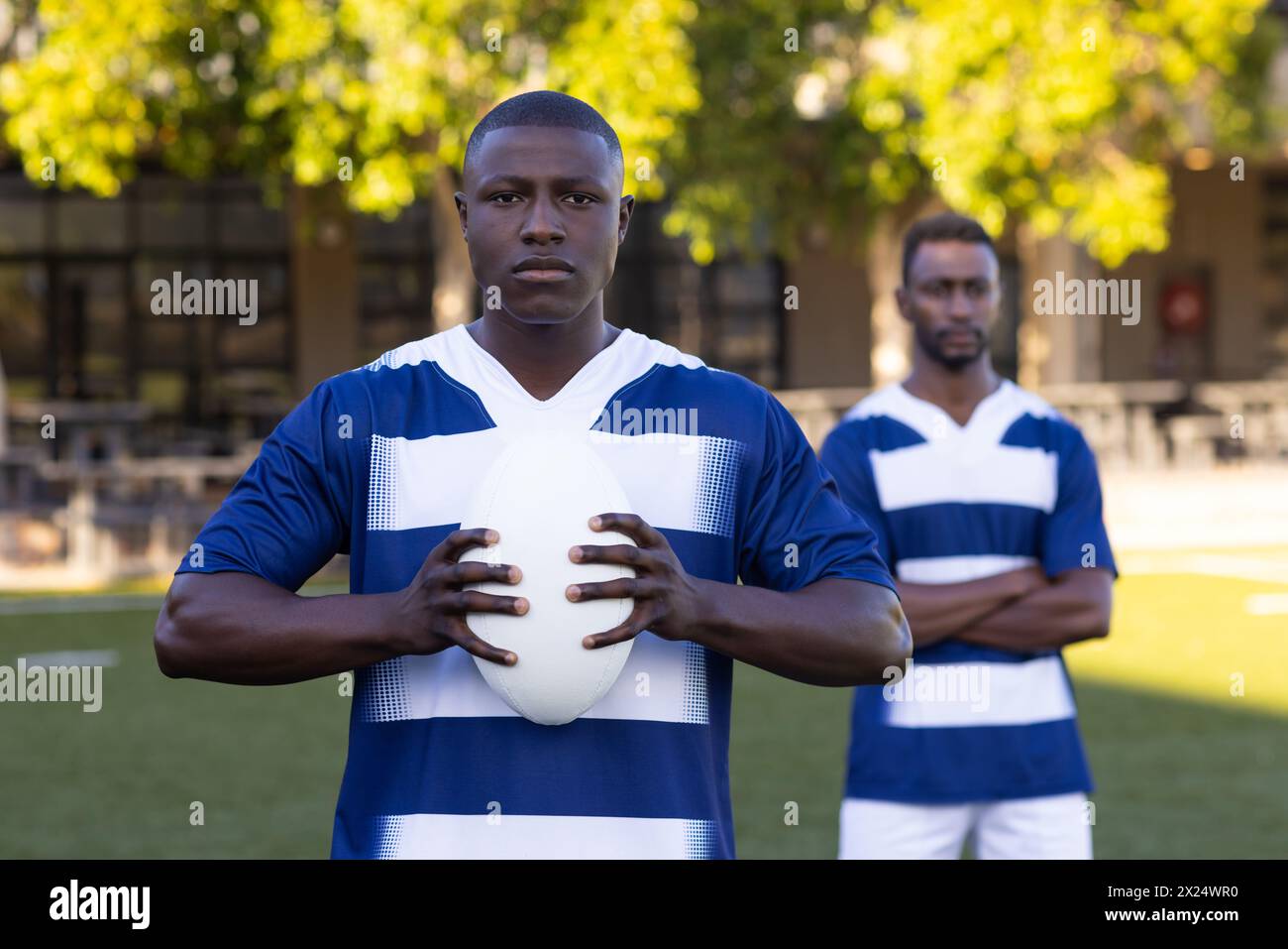 Due giovani atleti afroamericani stanno tenendo una palla di rugby in un campo all'aperto Foto Stock