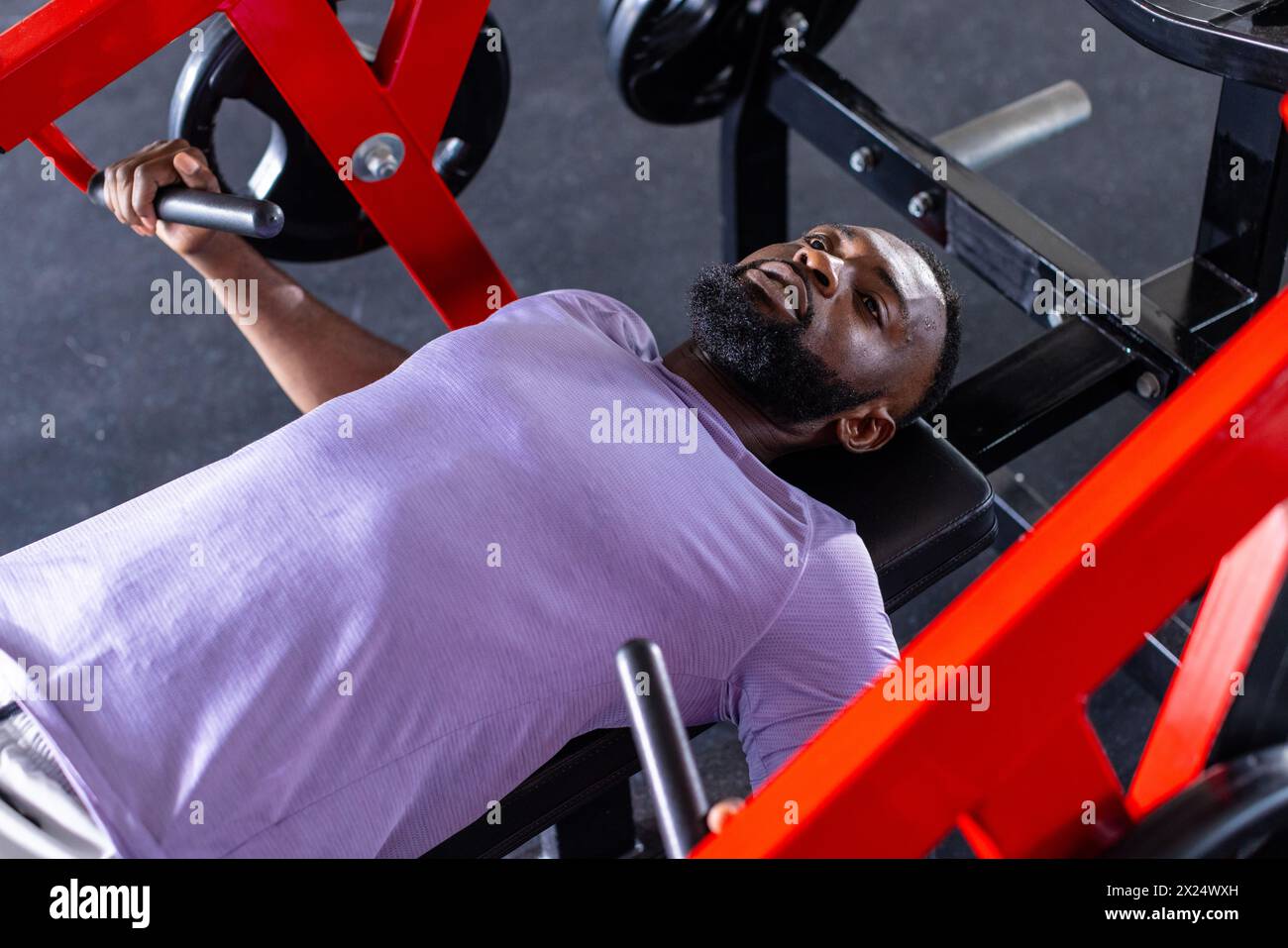 Un giovane atleta afroamericano, un modello di fitness sdraiato su una panchina in una palestra, che solleva pesi Foto Stock