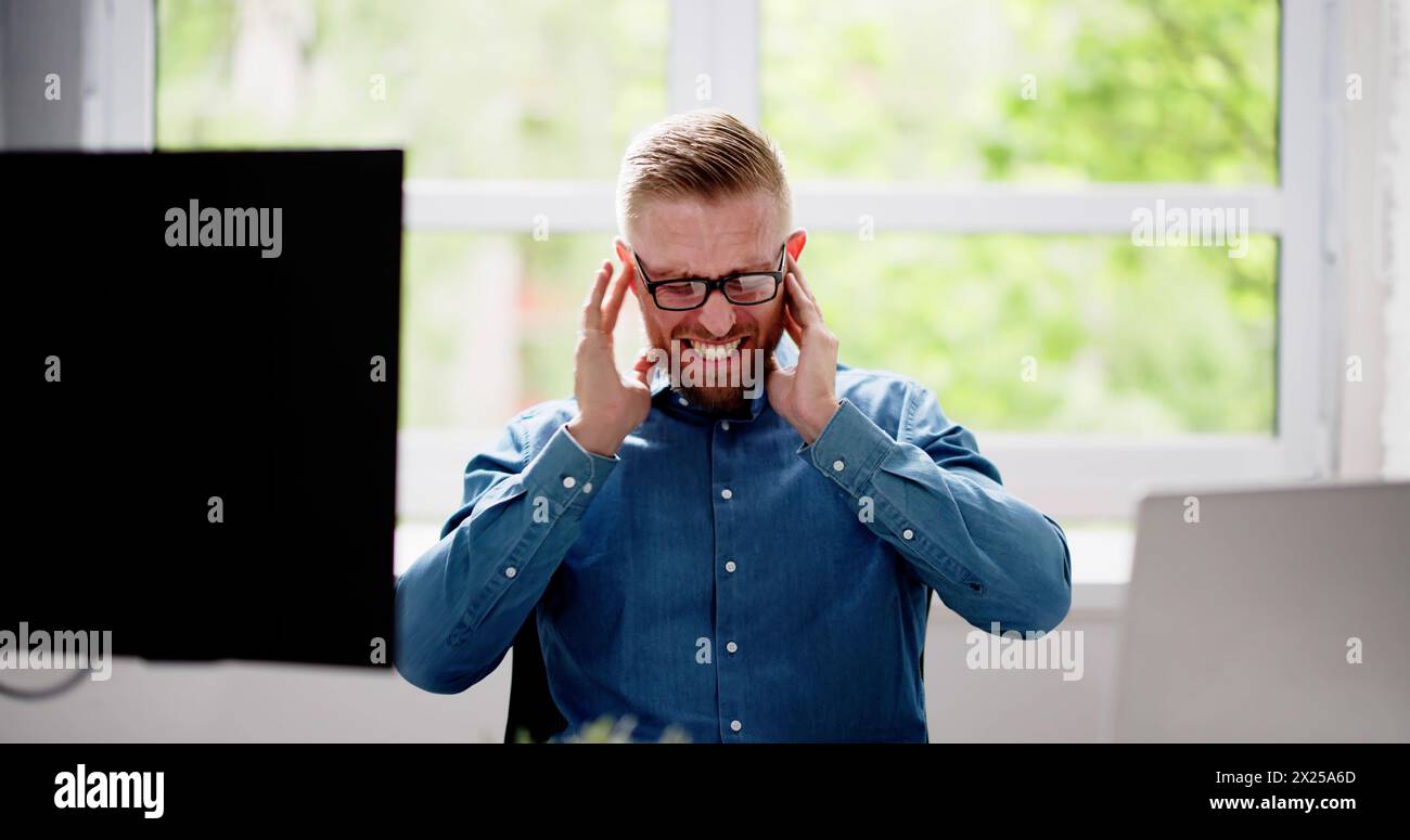 Uomo che copre l'orecchio con le mani in ufficio Foto Stock