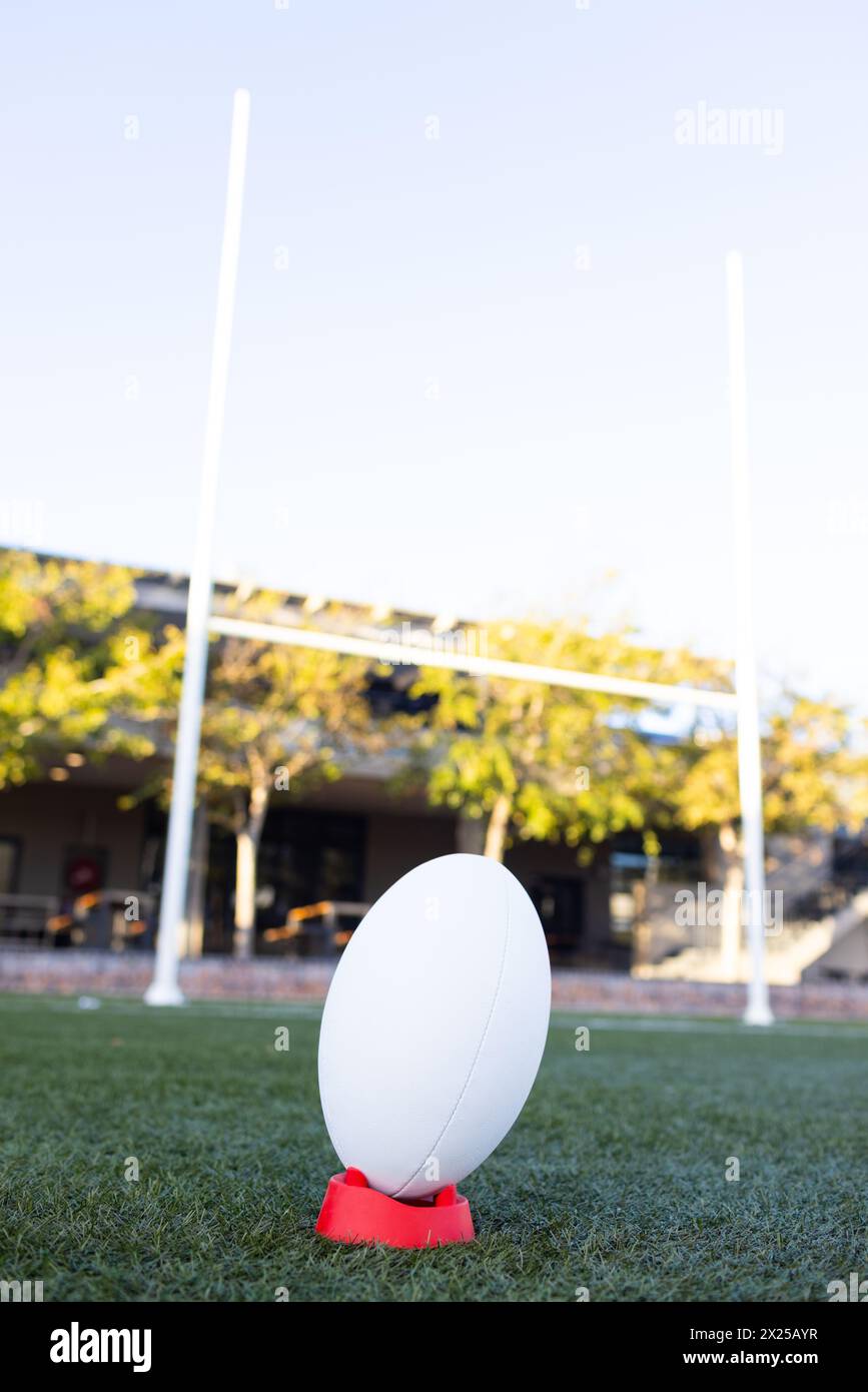 Palla da rugby su tee rosso con pali di Field goal dietro, copia spazio Foto Stock