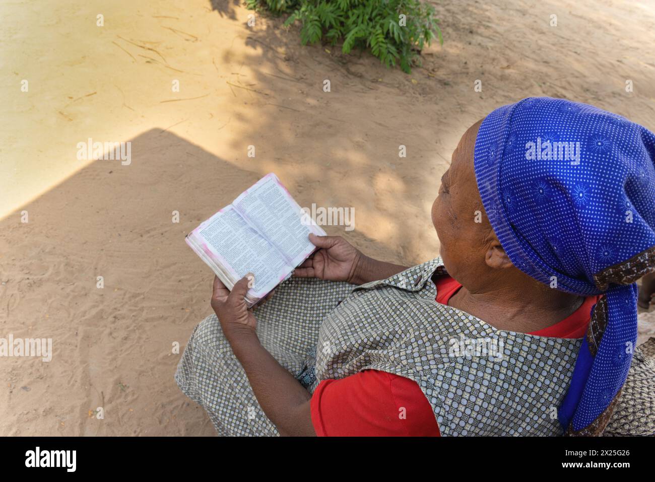 Vecchia donna africana cristiana del villaggio, che legge il libro sacro della bibbia, casual vestito con foulard blu Foto Stock